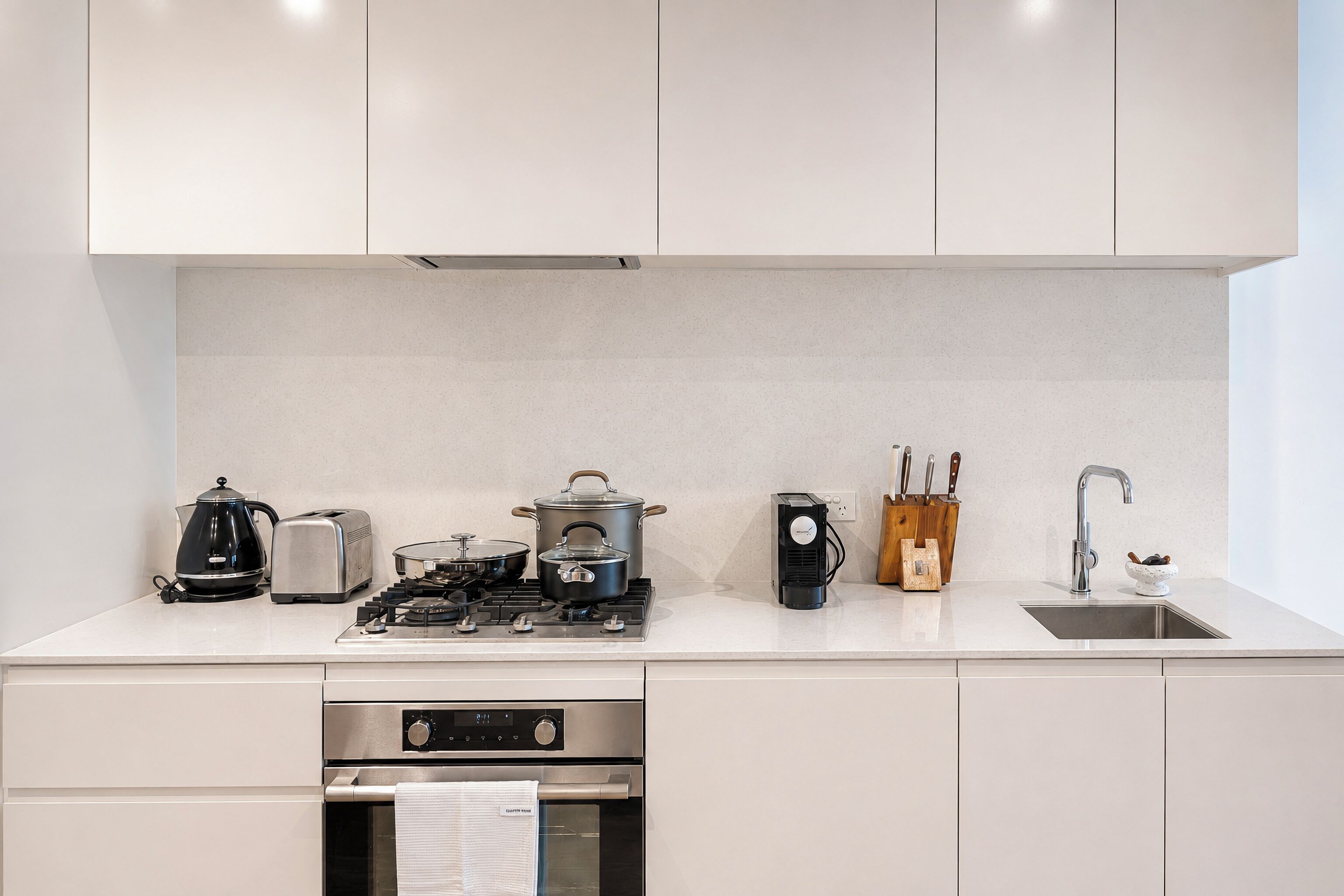 Eine moderne Küche mit weißen Schränken, einem Gasherd, einer Kaffeemaschine, einem Toaster, einem Wasserkocher, einem Messerblock und einer Spüle.