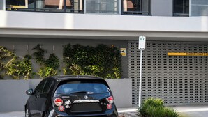 Um carro preto estacionado em uma vaga de estacionamento, com um edifício ao fundo.