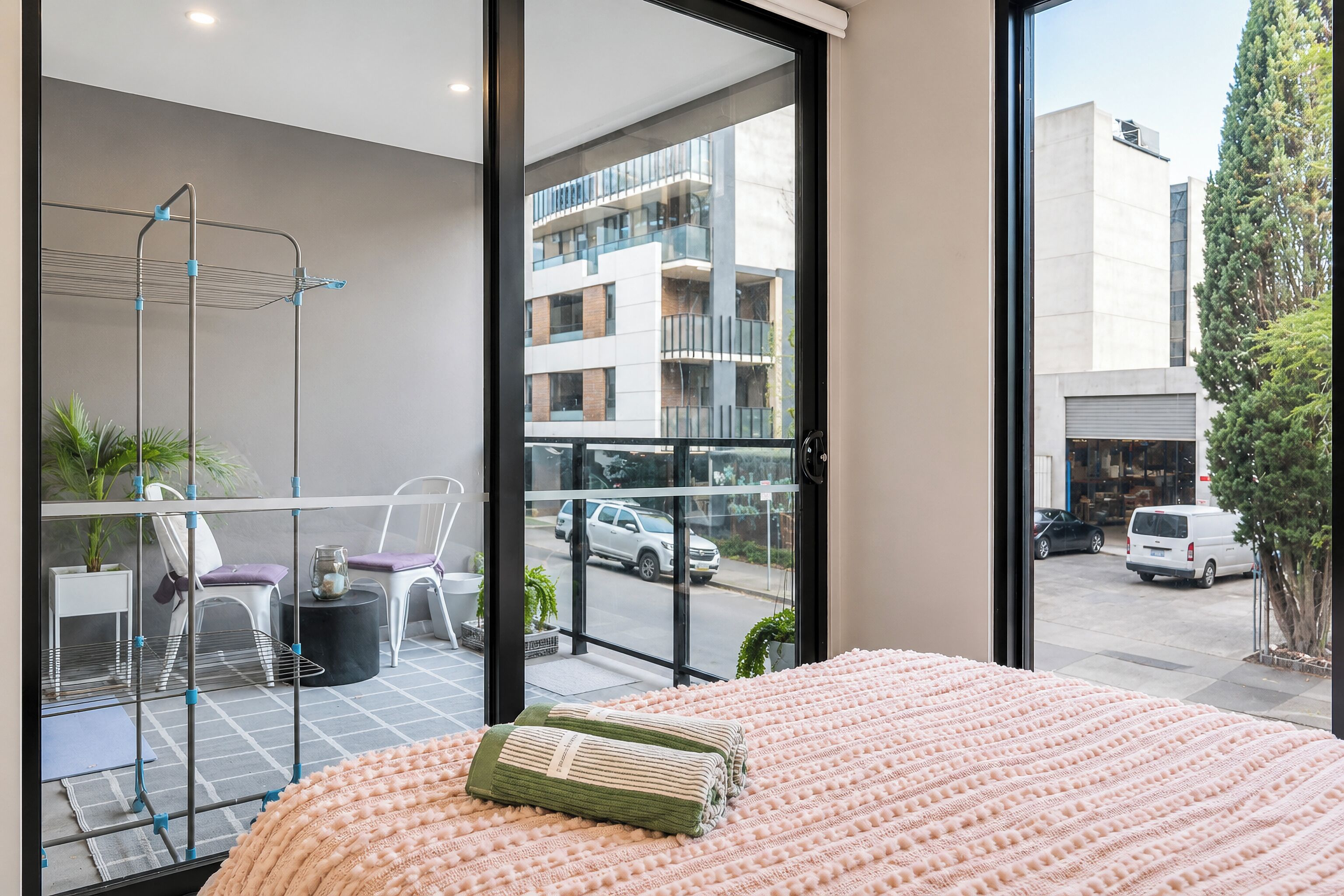 Une chambre moderne dotée d’un grand lit, d’un balcon avec un coin salon et d’une vue sur la rue et les immeubles.