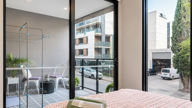 Quarto moderno com cama grande, varanda com área de estar e vista para a rua e edifícios.