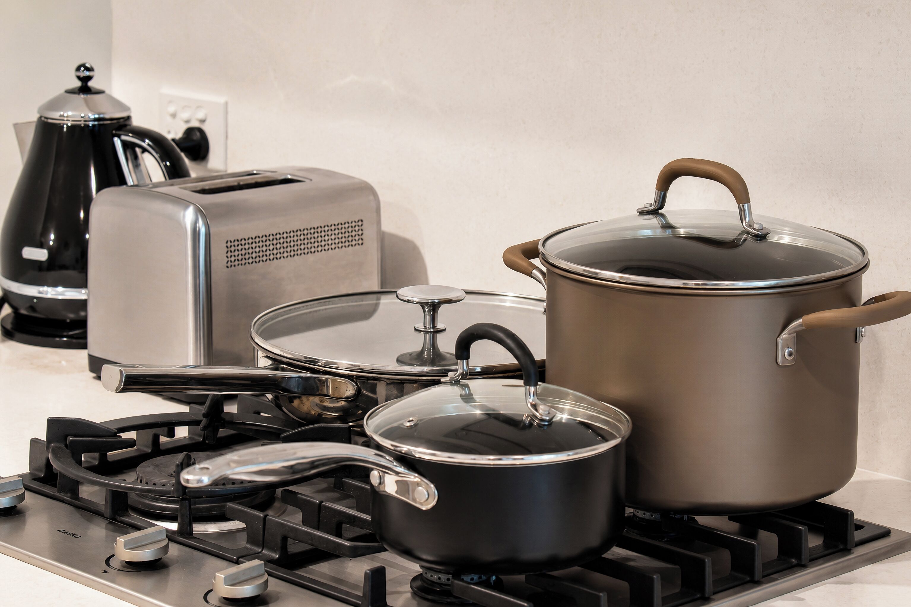 A kitchen with a gas stove, a toaster, a kettle, and a pot on the stove.