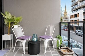 A balcony with two white chairs, a black table, and a glass vase. - Hawthorn 2BR Apartment | 2 Queen Beds | Balcony (Hawthorn)