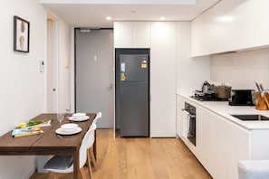 A compact kitchen with white cabinets, a built-in oven, and a dining area with a wooden table and chairs. - Hawthorn 2BR Apartment | 2 Queen Beds | Balcony (Hawthorn)