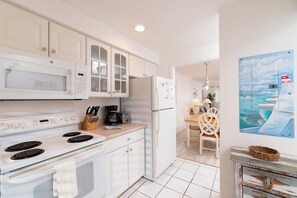A kitchen with white cabinets, a microwave, stove, and a refrigerator. There is a dining area with a table and chairs. - Nautilus 205 by Nautilus Vacations-Beachfront Complex, Pool, Recreation Court (Holmes Beach)