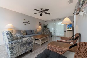 Ein Wohnzimmer mit einer Couch, zwei Sesseln, einem Couchtisch, einem Deckenventilator und Wanddekoration.