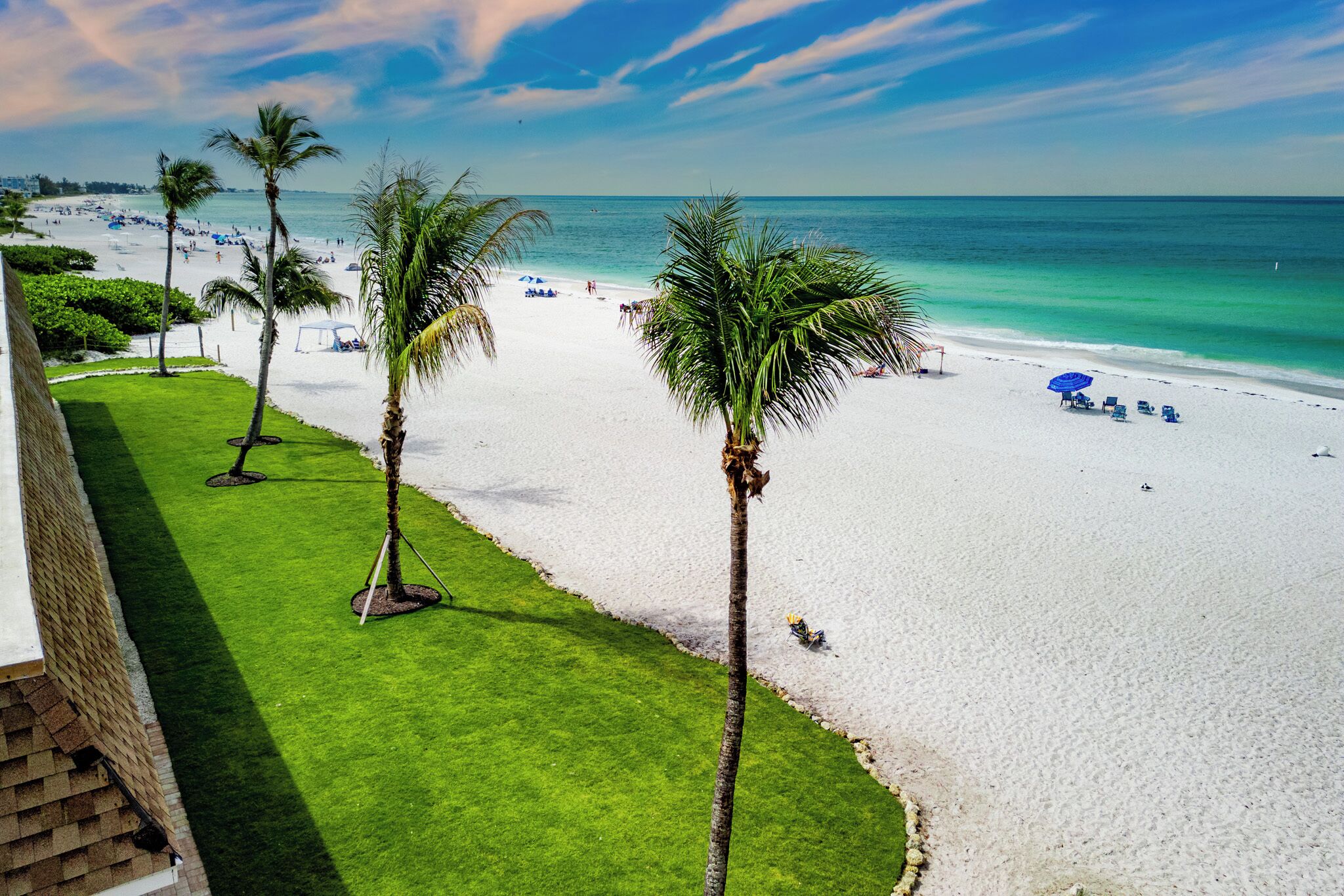 A beach with white sand, palm trees, and a clear blue sky.