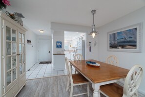 Ein Essbereich mit Holztisch und -stühlen, eine Küche im Hintergrund und ein Gang zu einem weiteren Raum.