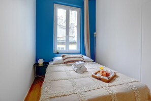 A bedroom with a bed, a bedside table, a window, and a tray of breakfast items. - Cozy 2BR in Le Marais & Montorgueil Location (Paris)