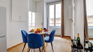 Un comedor con una mesa dispuesta para dos, sillas azules, una araña y una ventana con cortinas.