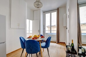 Ein Essbereich mit einem für zwei gedeckten Tisch, blauen Stühlen, einer Kristallleuchter und einem Fenster mit Vorhängen.