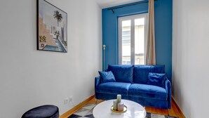 Una habitación con un sofá azul, una mesita redonda con velas, un otoman negro y un cuadro en la pared.