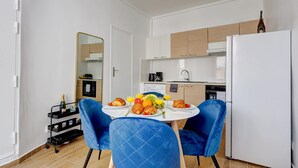 Una cocina moderna con armarios blancos, un refrigerador blanco y una mesa de comedor dispuesta con cruasanes, fruta y jugo.