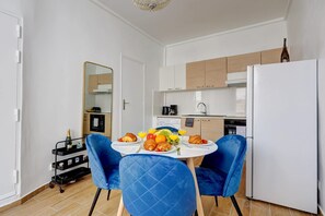 Eine moderne Küche mit weißen Schränken, einem weißen Kühlschrank und einem Esstisch, gedeckt mit Croissants, Obst und Saft.