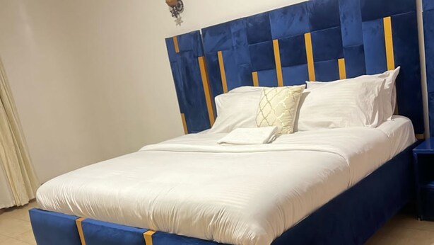 A bed with a blue headboard and footboard, white bedding, and a small bedside table. - Imagine Luxury View Palace Apartment (Nairobi)