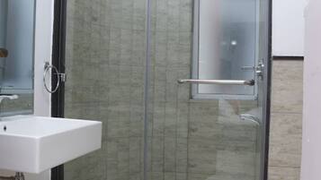 Un baño con cabina de ducha de vidrio, un lavamanos blanco y un espejo.
