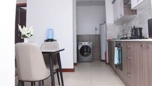 A compact kitchen with a washing machine, a dining area with a chair, and a small table. - Imagine Luxury View Palace Apartment (Nairobi)