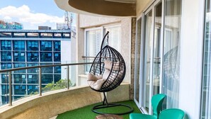 A balcony with artificial grass, a hanging chair, two round tables, and green chairs. - Imagine Luxury View Palace Apartment (Nairobi)
