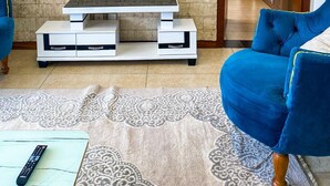 A living room with a flat-screen TV mounted on a stone wall, a white entertainment unit, a blue sofa, and a patterned rug. - Imagine Luxury View Palace Apartment (Nairobi)