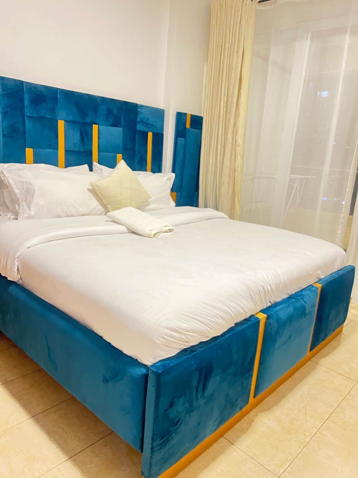 Una cama con cabecera azul y ropa de cama blanca, una almohada blanca y una toalla blanca doblada.