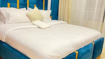 Una cama con cabecera azul y ropa de cama blanca, una almohada blanca y una toalla blanca doblada.