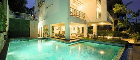 A swimming pool with a tiled edge, surrounded by a building with multiple balconies and outdoor seating areas.