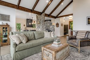 Ein geräumiges Wohnzimmer mit Steinwand, Holzboden und einer gemütlichen Sitzecke mit Sofa und Sessel.