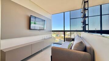 A modern living room with a sofa, a mounted TV, and a view of the city through large windows.