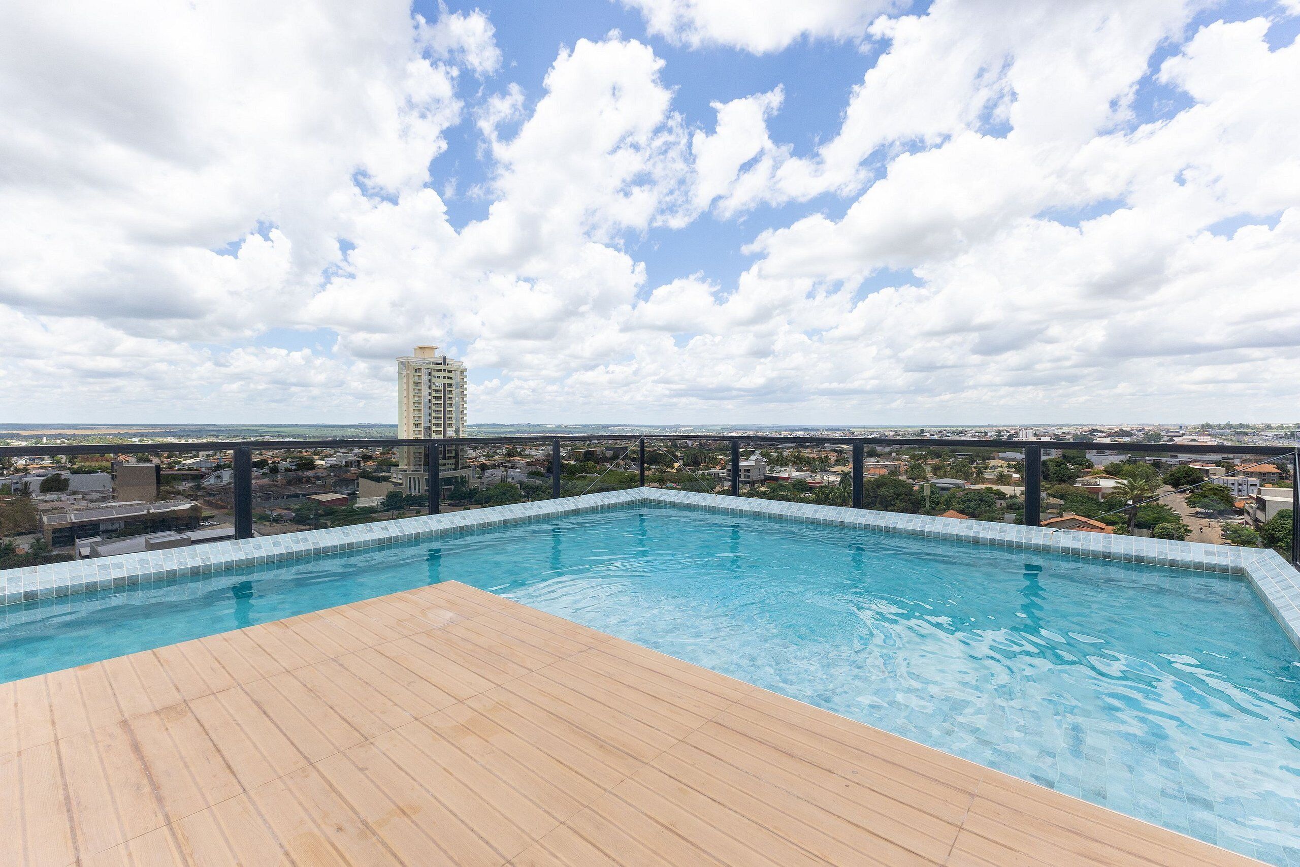 Ein Pool auf dem Dach mit einer Holzterrasse und Blick auf eine Stadtlandschaft sowie ein hohes Gebäude in der Ferne.