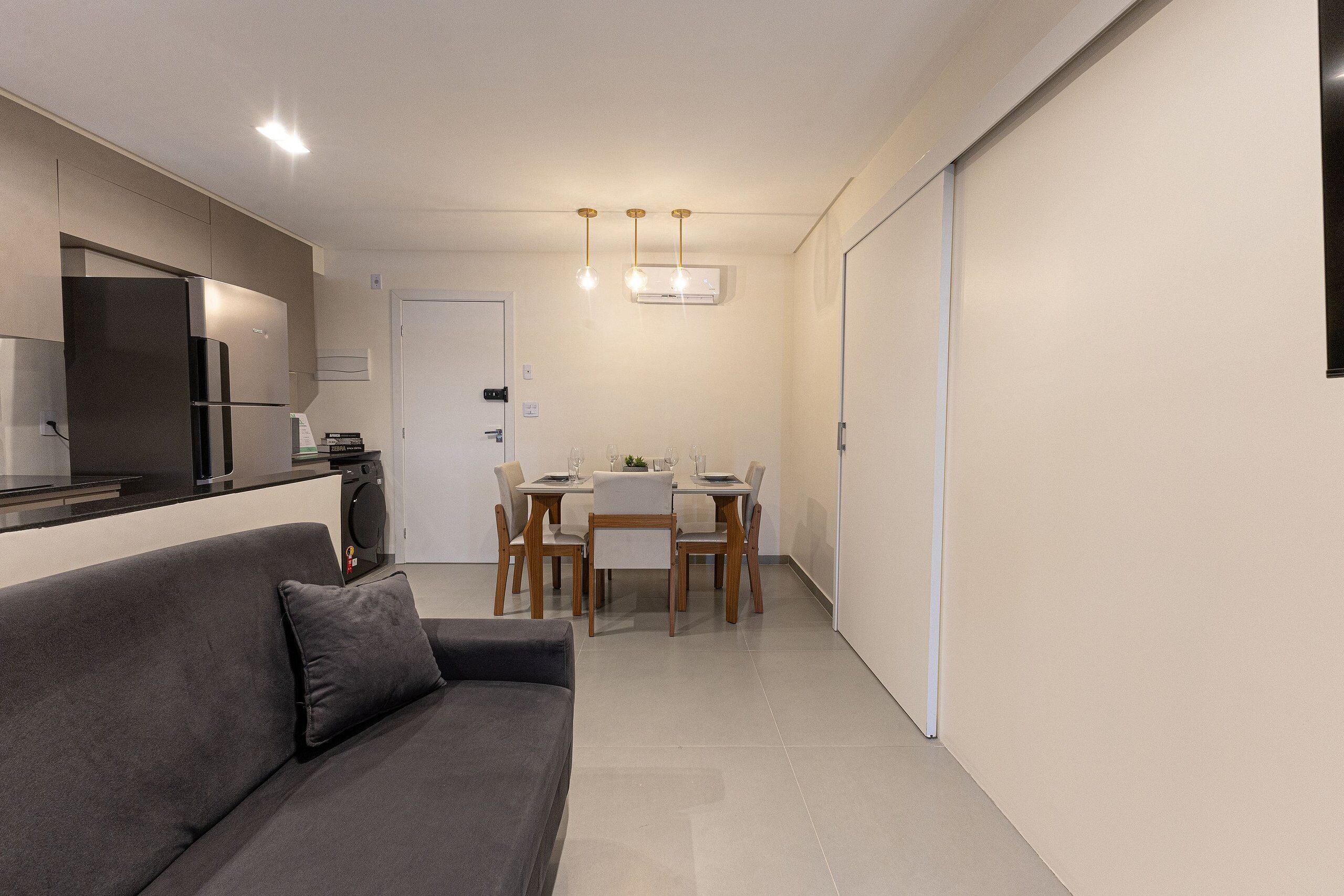 A compact living space with a sofa, a dining table with chairs, a kitchen area with appliances, and a sliding door.
