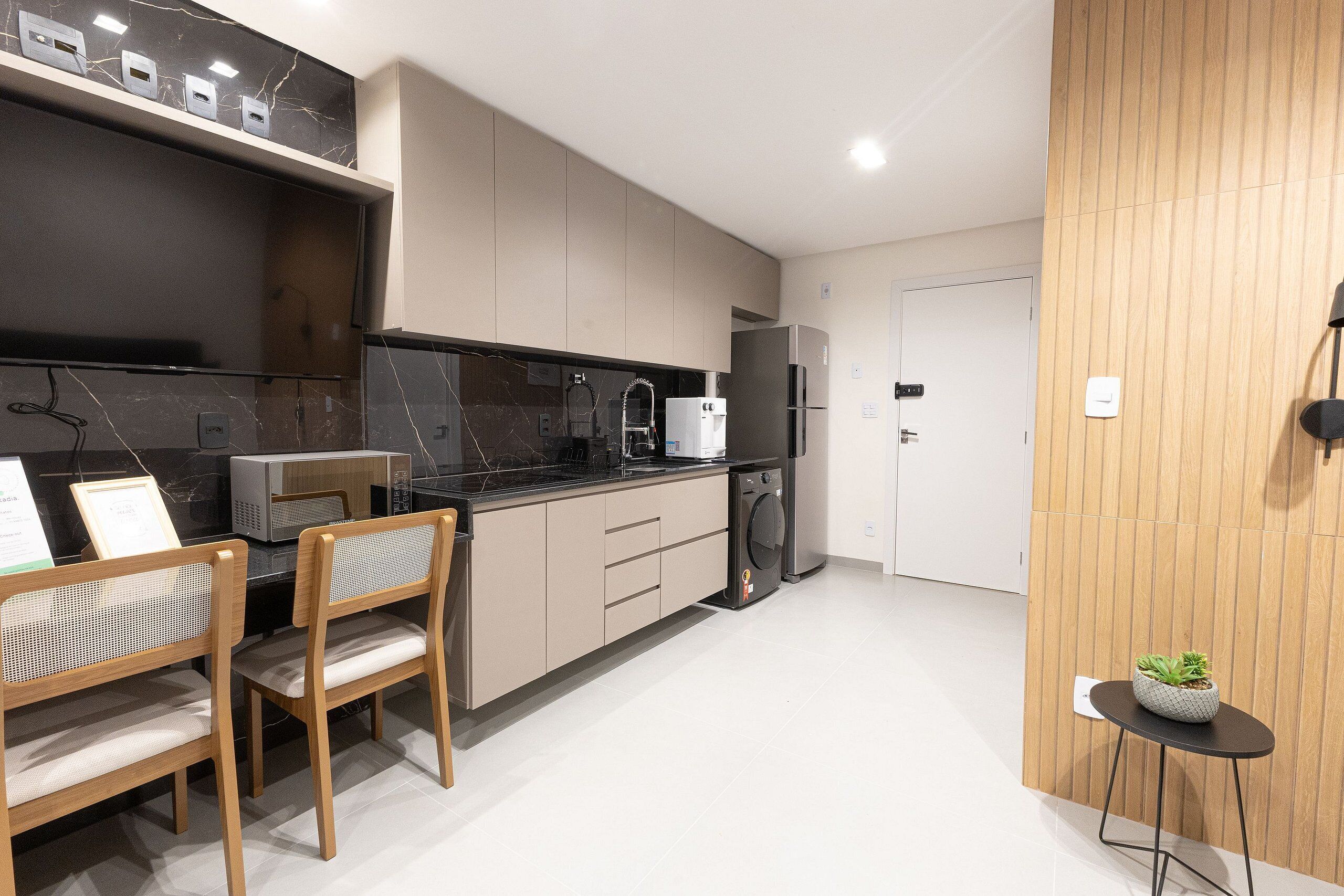 A modern kitchen with a built-in stove, a refrigerator, and a sink. There are two wooden chairs and a small table with a plant.