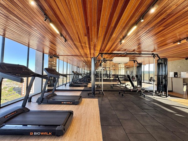 Un gimnasio con cintas de correr, máquinas de pesas y un amplio ventanal con vistas a la ciudad.