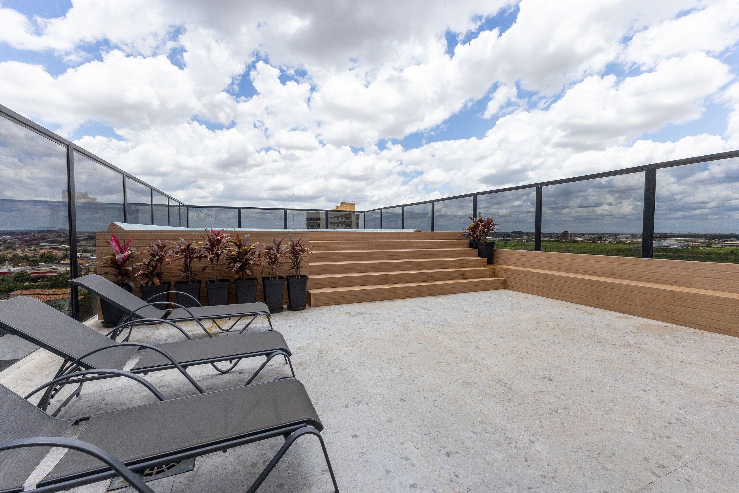 Una terraza en la azotea con vistas a la ciudad, una escalera que conduce a un nivel superior y mobiliario exterior.