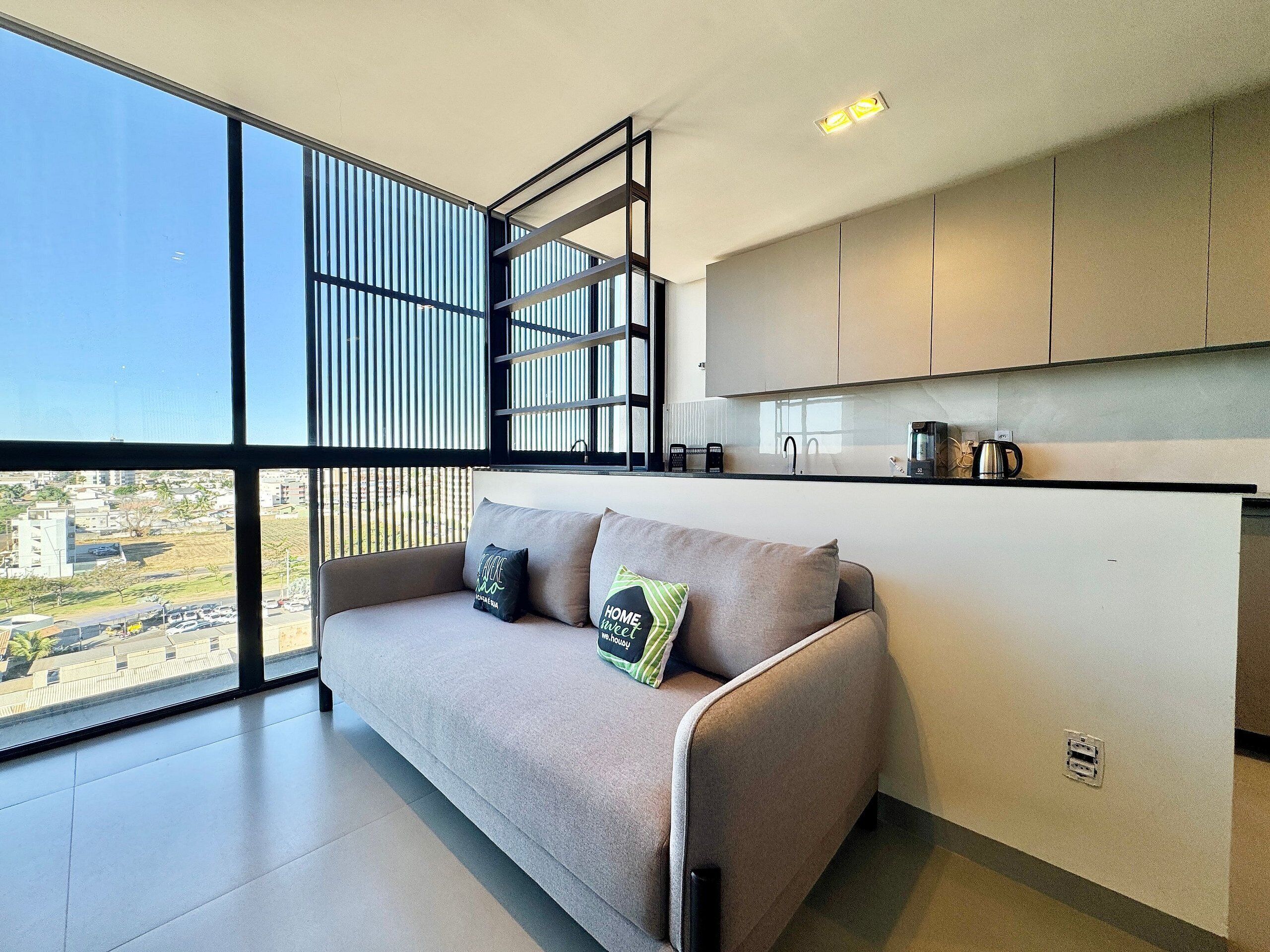 A modern living space with a sofa, a kitchen area, and a view of the city.