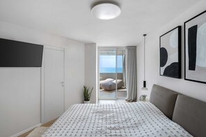 A bedroom with a bed, a TV, a balcony with a view, and artwork on the wall. - Bright Oceanfront Penthouse | Panoramic Sea Views (hertzelya)