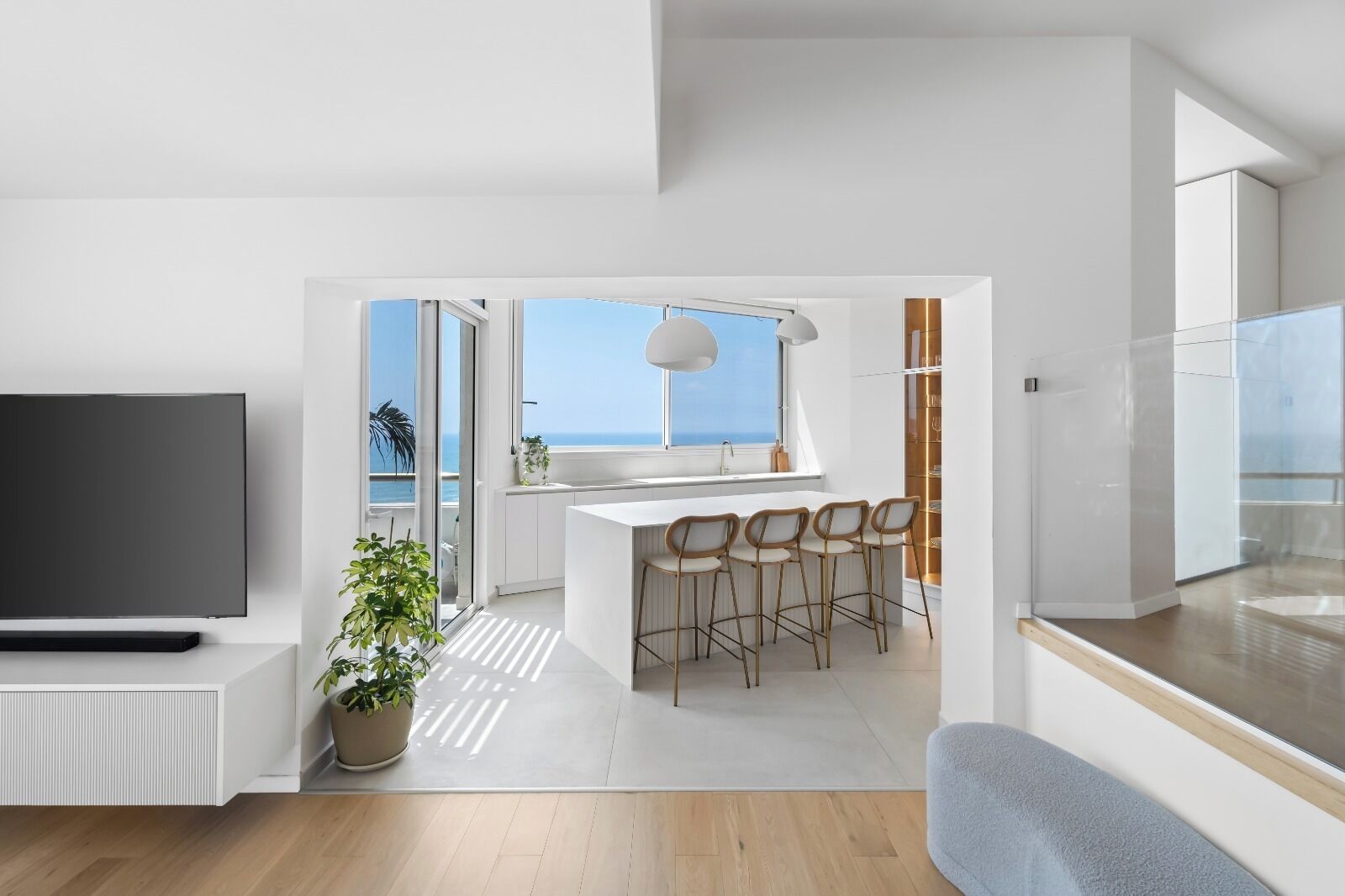 Un salon moderne doté d’un téléviseur à écran plat, d’une plante en pot et offrant une vue sur l’océan grâce à de grandes fenêtres.