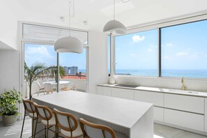 A modern kitchen with a large island, white cabinetry, and a view of the ocean. - Bright Oceanfront Penthouse | Panoramic Sea Views (hertzelya)