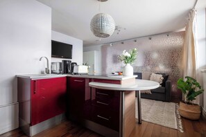 A modern kitchen with a red and white color scheme, a round dining table, and a decorative plant. - 1BR by Piccadilly Circus & Trafalgar Square (London)