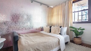 A bedroom with a bed, a bedside table, a potted plant, and a window with curtains. - 1BR by Piccadilly Circus & Trafalgar Square (London)