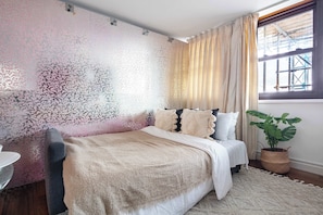 A bedroom with a bed, a bedside table, a potted plant, and a window with curtains. - 1BR by Piccadilly Circus & Trafalgar Square (London)