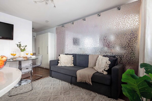 A modern living room with a dark grey sofa, a glass coffee table, and a patterned wall. - 1BR by Piccadilly Circus & Trafalgar Square (London)
