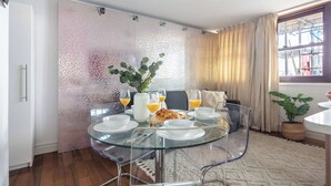 A dining area with a glass table set for four, surrounded by a patterned wall and a window with curtains. - 1BR by Piccadilly Circus & Trafalgar Square (London)