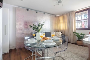 A dining area with a glass table set for four, surrounded by a patterned wall and a window with curtains. - 1BR by Piccadilly Circus & Trafalgar Square (London)