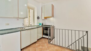 Una cucina con mobili bianchi, un lavello in acciaio inossidabile, un fornello e una ringhiera nera.