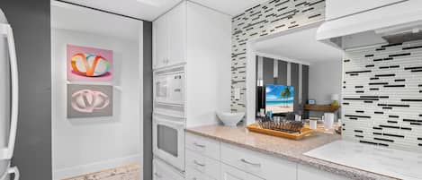 Cocina moderna con muebles blancos, microondas, horno e isla grande con un bol y utensilios.