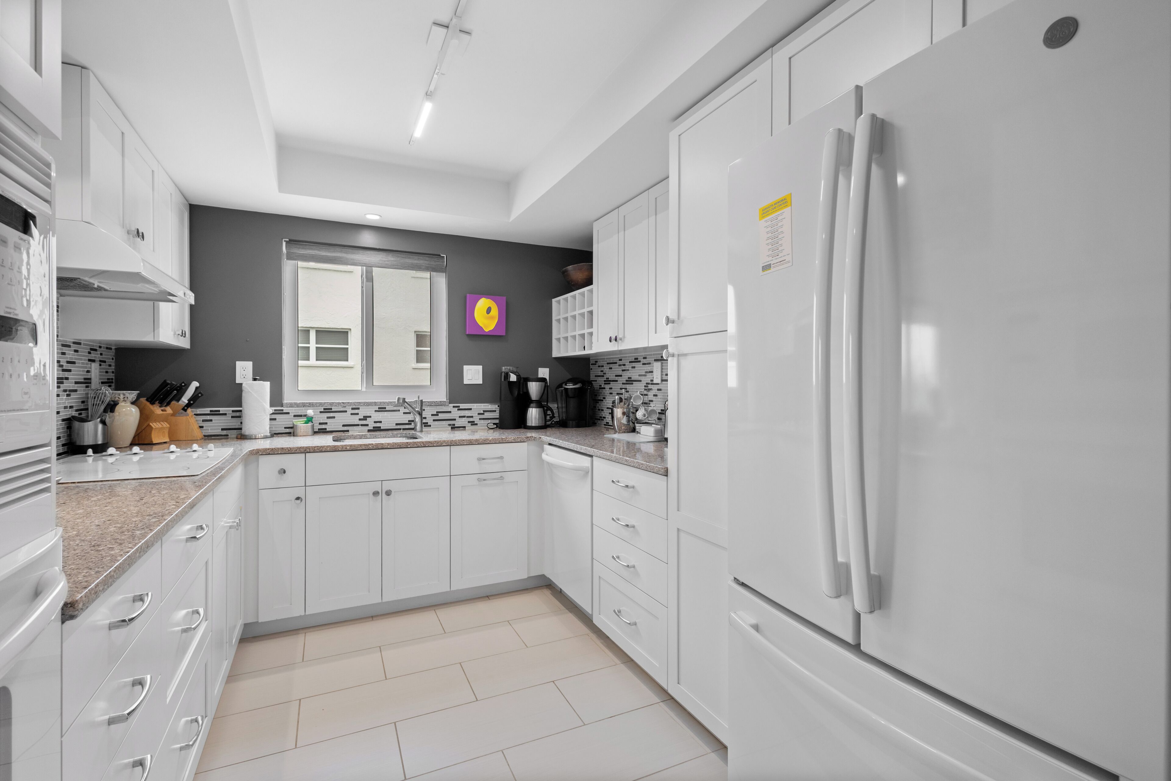 Una cocina moderna con armarios blancos, un refrigerador de acero inoxidable y un salpicadero de azulejos.