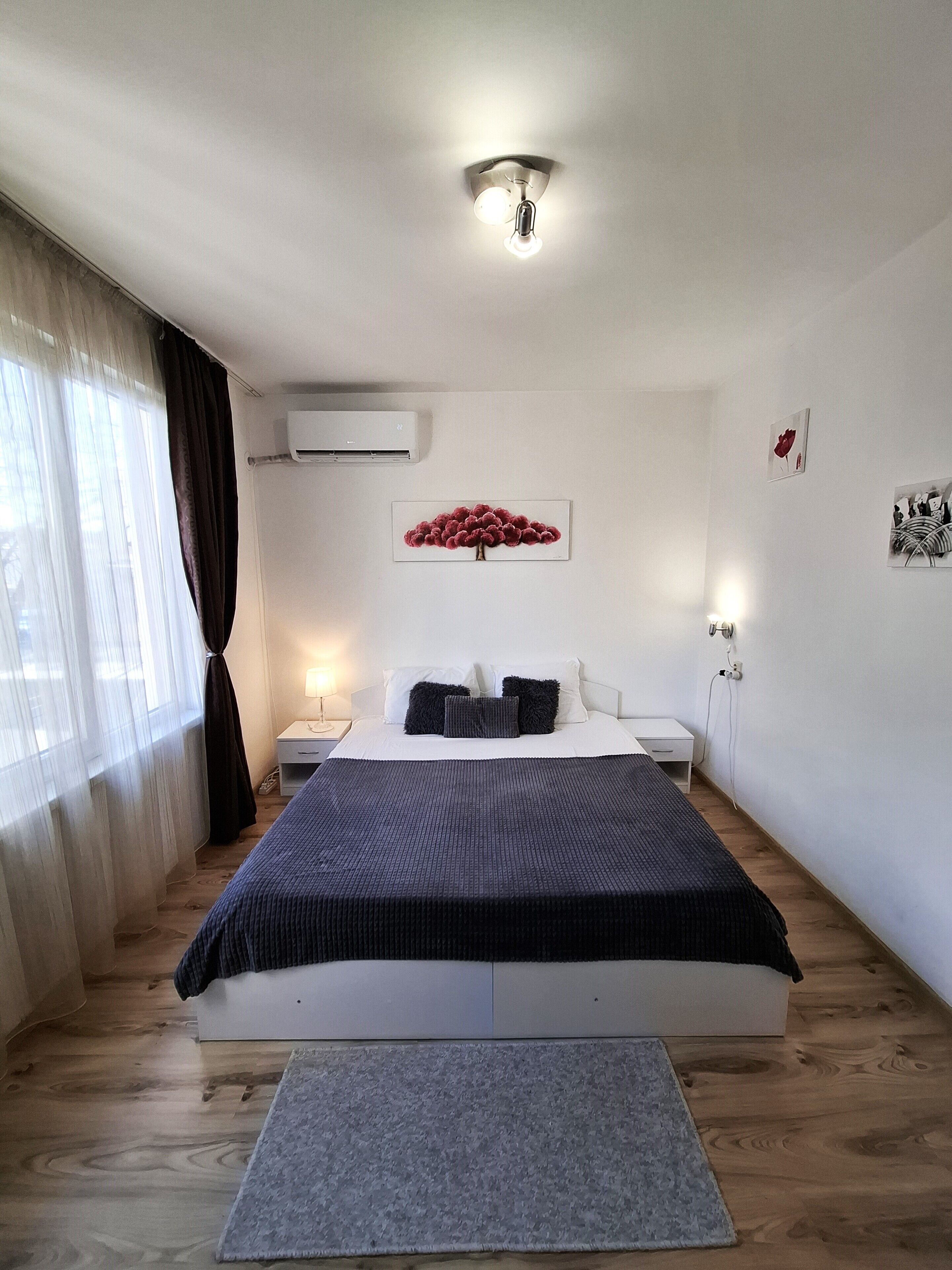 Une chambre moderne avec un grand lit, une table de chevet, un appareil de climatisation, un luminaire fixé au mur et une œuvre d’art encadrée.