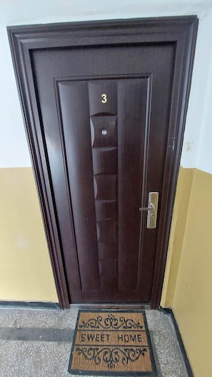 A dark wooden door with a number '3' above it, a metal handle, and a doormat with 'SWEET HOME' written on it.