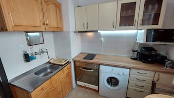 A compact kitchen with wooden cabinets, a stainless steel sink, a built-in oven, a dishwasher, and a microwave.