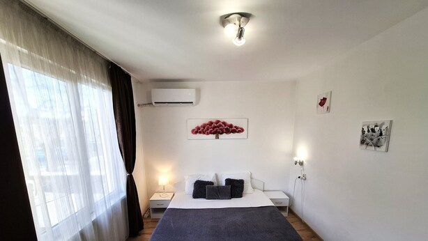 A bedroom with a bed, bedside tables, an air conditioning unit, and artwork on the walls.