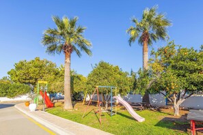 Ein Spielplatz mit Schaukeln und Rutschen, umgeben von Palmen und viel Grün.
